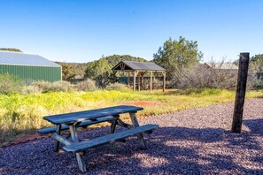 A picnic table in a gravel area with a metal roof structure and a green building in the background. - Private Indoor Pickleball Court Red Rock Views (Sedona)