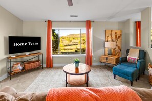 Een woonkamer met een televisie, uitzicht op een landschap, een bank, een fauteuil en een plantentafel.