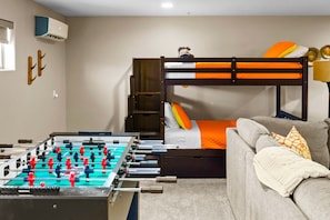 A room with a bunk bed, a foosball table, a sofa, and a wall-mounted air conditioner. - Private Indoor Pickleball Court Red Rock Views (Sedona)