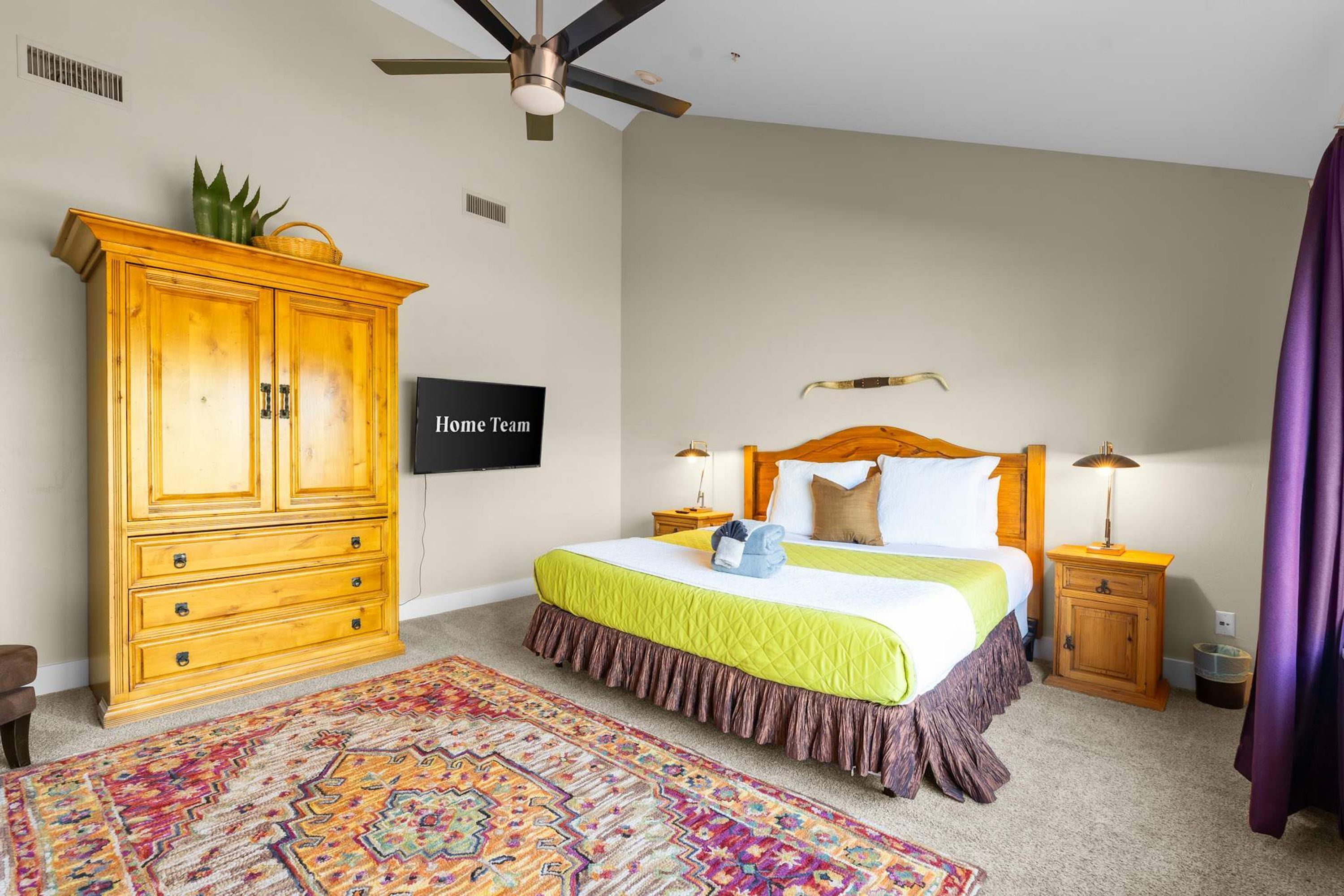 A bedroom with a bed, a wooden cabinet, a television, and a ceiling fan.