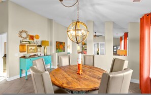 A dining room with a round wooden table, six chairs, a chandelier, and a teal accent wall. - Private Indoor Pickleball Court Red Rock Views (Sedona)