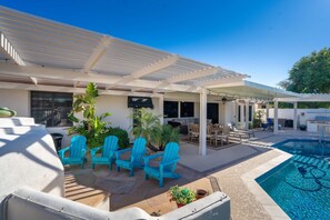 A covered outdoor area with a pool, seating, and potted plants. - Pool Spa Outdoor Fireplace BBQ Pool Table (Goodyear)