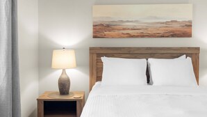 A hotel room with a bed, a nightstand with a lamp, and a painting on the wall. - Pool Spa Outdoor Fireplace BBQ Pool Table (Goodyear)