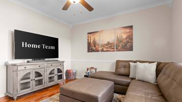 A living room with a brown leather sofa, a television, a cabinet, and a wall with a desert landscape painting.