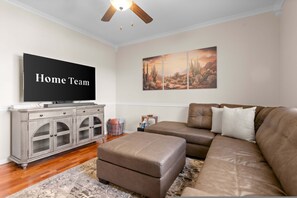A living room with a brown leather sofa, a television, a cabinet, and a wall with a desert landscape painting. - Pool Spa Outdoor Fireplace BBQ Pool Table (Goodyear)