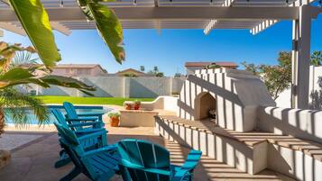 A covered outdoor area with a barbecue, seating, and a view of a residential neighborhood.