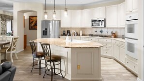 A modern kitchen with white cabinetry, a central island with bar stools, stainless steel appliances, and pendant lighting. - Pool Spa Outdoor Fireplace BBQ Pool Table (Goodyear)