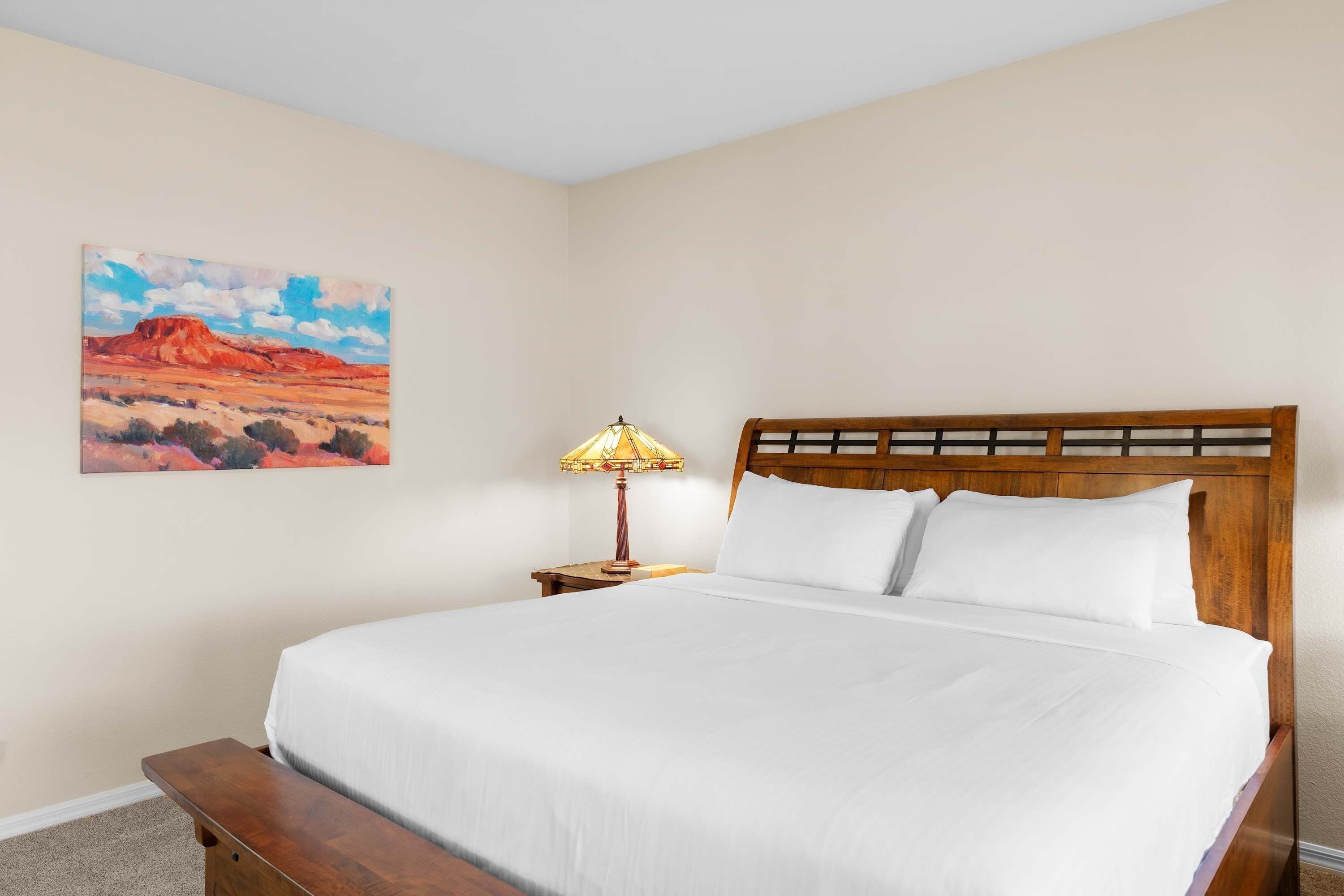 A hotel room with a bed, a nightstand, a lamp, and a painting on the wall.