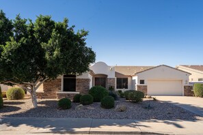 A two-story house with a stone facade, a garage, and a well-maintained front yard with various shrubs and a large tree. - Pool Spa Outdoor Fireplace BBQ Pool Table (Goodyear)