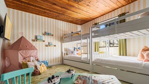 Une chambre d’enfant avec des lits superposés, un espace de jeux avec des jouets et un mur à rayures.