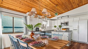 Une cuisine moderne avec des meubles blancs, une table à manger en bois prévue pour quatre personnes et une vue sur la mer par une grande fenêtre.