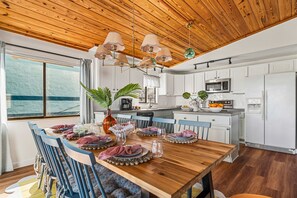 A modern kitchen with white cabinets, a wooden dining table set for four, and a view of the sea through a large window. - Ocean Views Private Pool Walk to Beach (St. Augustine)