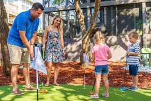 A family playing golf on a manicured lawn with a modern building in the background. - Ocean Views Private Pool Walk to Beach (St. Augustine)
