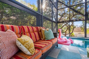 Ein sonnendurchflutetes Zimmer mit einem gestreiften Sofa, Kissen und einem Pool mit aufblasbaren Flamingos.