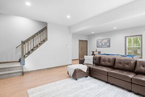 Ein geräumiges Wohnzimmer mit einem braunen Ledersofa, einer Holztreppe, einem Billardtisch und einer Weltkarte an der Wand.