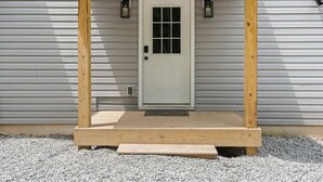 Una puerta principal con un porche de madera, dos faroles fijados a la pared y un camino de entrada de grava.