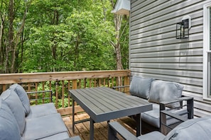 A deck with a table and two sofas, surrounded by a wooden railing, overlooking a forested area. - Sleeps 16 Hot Tub Arcade Resort Amenities (Albrightsville)
