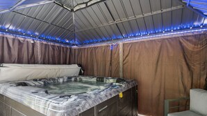Un jacuzzi con revestimiento tipo mármol, techo con iluminación LED azul y un telón de fondo de cortina marrón.