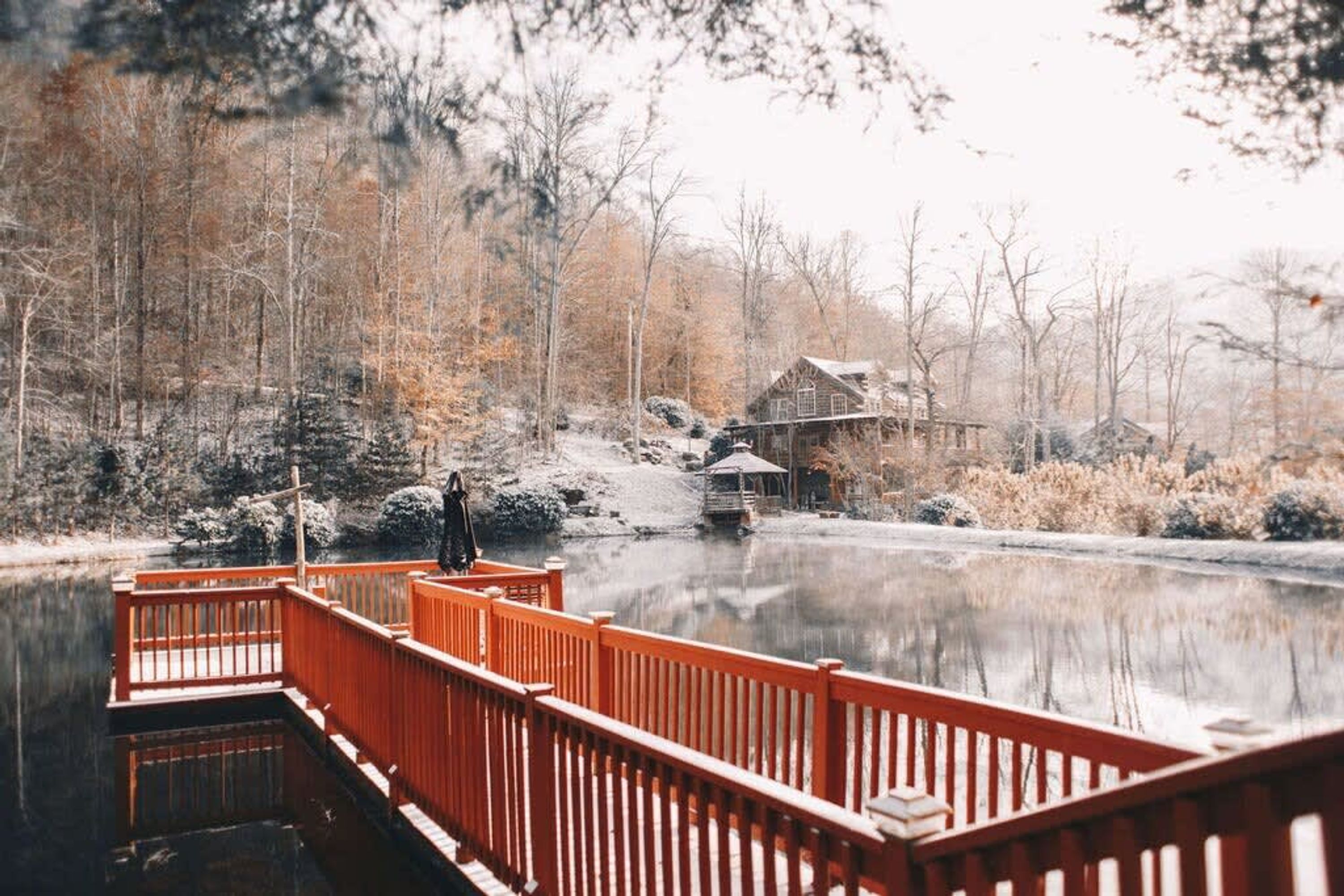 A wooden dock extending over a calm lake, surrounded by trees and a rustic cabin.