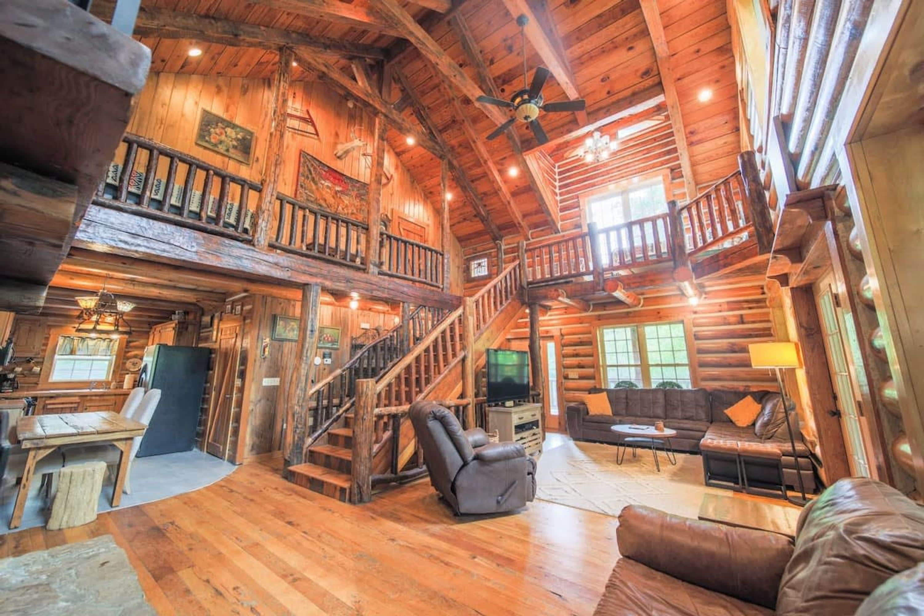 A spacious log cabin interior with a central staircase, a cozy seating area, and a television.