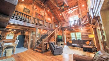 A spacious log cabin interior with a central staircase, a cozy seating area, and a television.