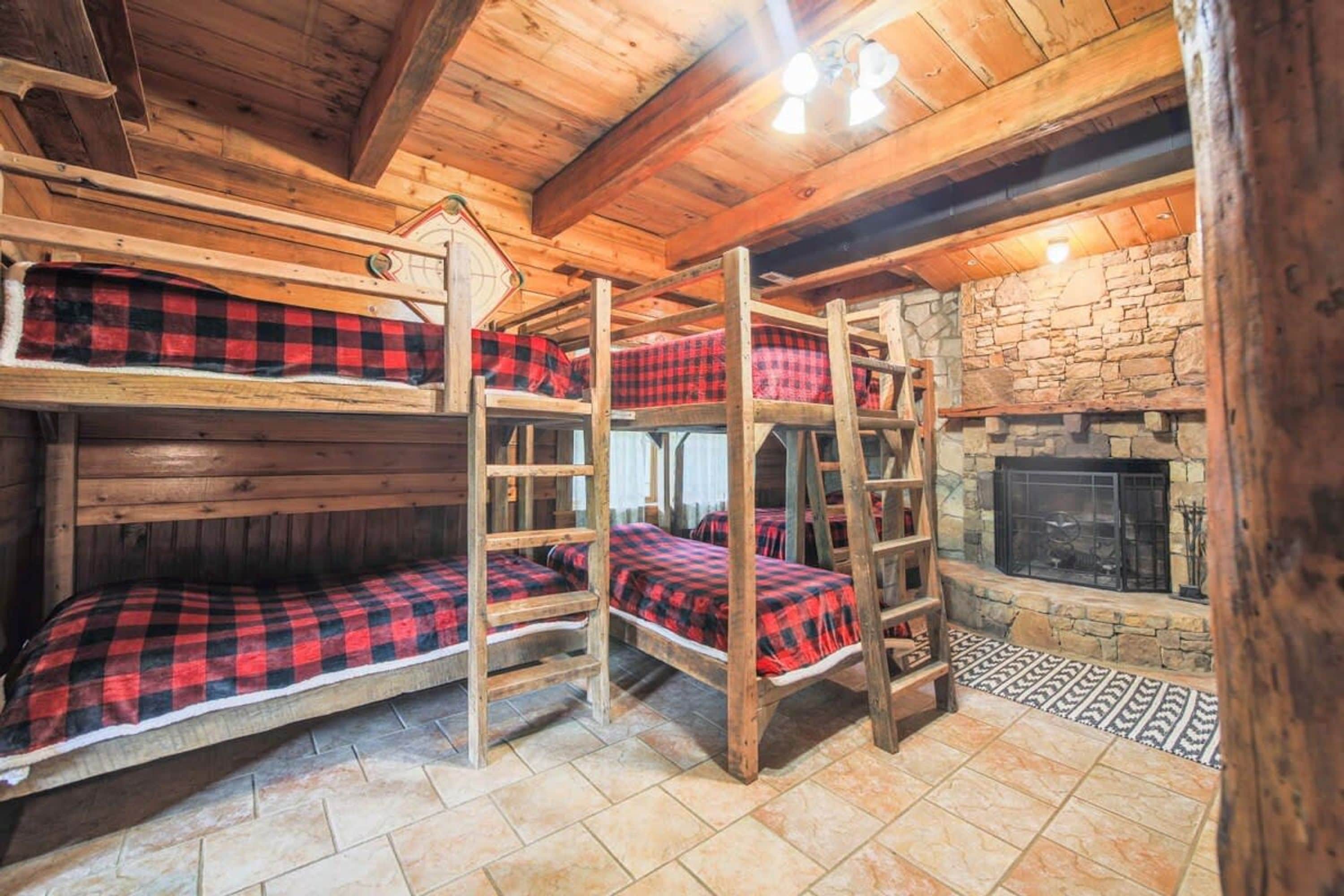 A bunk bed room with a stone fireplace and wooden beams.