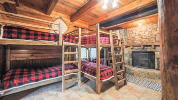 A bunk bed room with a stone fireplace and wooden beams.