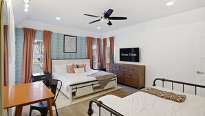Un dormitorio con cama, escritorio, silla, cómoda, televisor y ventilador de techo.
