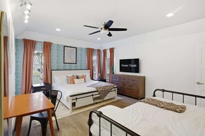 Ein Schlafzimmer mit Bett, Schreibtisch, Stuhl, Kommode, Fernseher und Deckenventilator.