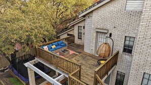 Una terraza de madera con un sofá azul y una silla colgante, un trampolín y un edificio de ladrillo con ventanas.