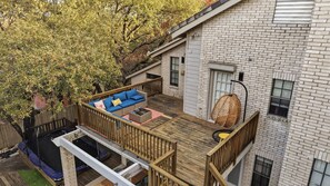 Eine Holzterrasse mit einem blauen Sofa, einem Hängesessel, einem Trampolin und einem Ziegelgebäude mit Fenstern.