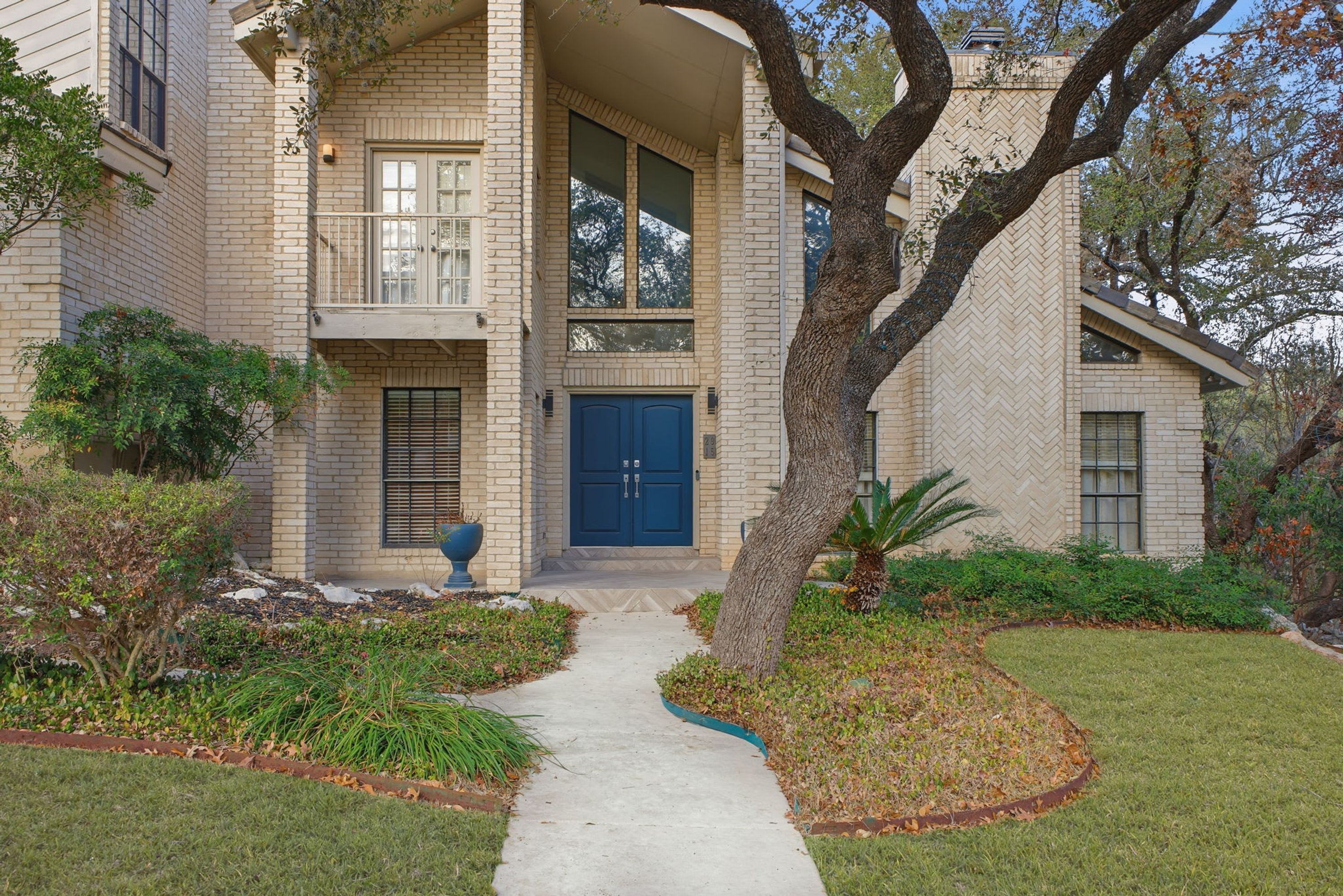 A two-story house with a front entrance, a covered porch, and a large tree in the front yard.