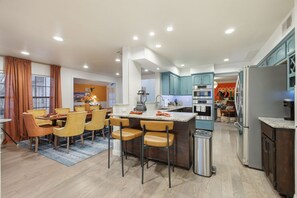 A modern kitchen with a central island, built-in appliances, and a dining area with yellow chairs. - Backyard Paradise - Pool - Tree House - Hot Tub (San Antonio)