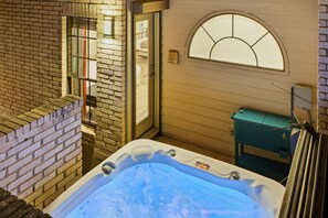 A hot tub in a corner with a brick wall and a window.