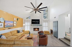 A modern living room with a sofa, armchairs, a coffee table, a fireplace, and a ceiling fan. - Backyard Paradise - Pool - Tree House - Hot Tub (San Antonio)