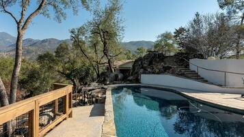 A swimming pool with a wooden deck and stone steps leading to a house.
