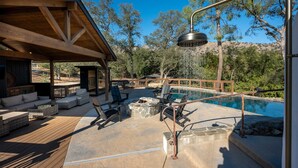 A covered outdoor area with a pool, lounge chairs, and a stone fire pit. - Sequoia Getaway Private Pool Sauna (Three Rivers)