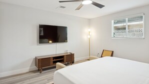 Ein Schlafzimmer mit einem Bett, einem Fernseher, einem Deckenventilator, einem Nachttisch und einem Fenster mit Jalousien.