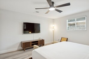 Ein Schlafzimmer mit einem Bett, einem Fernseher, einem Deckenventilator, einem Nachttisch und einem Fenster mit Jalousien.
