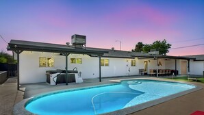 Ein Wohnhausgarten mit Schwimmbad, Sitzgelegenheiten und einer überdachten Terrasse.