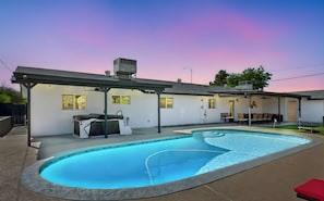 Ein Wohnhausgarten mit Schwimmbad, Sitzgelegenheiten und einer überdachten Terrasse.