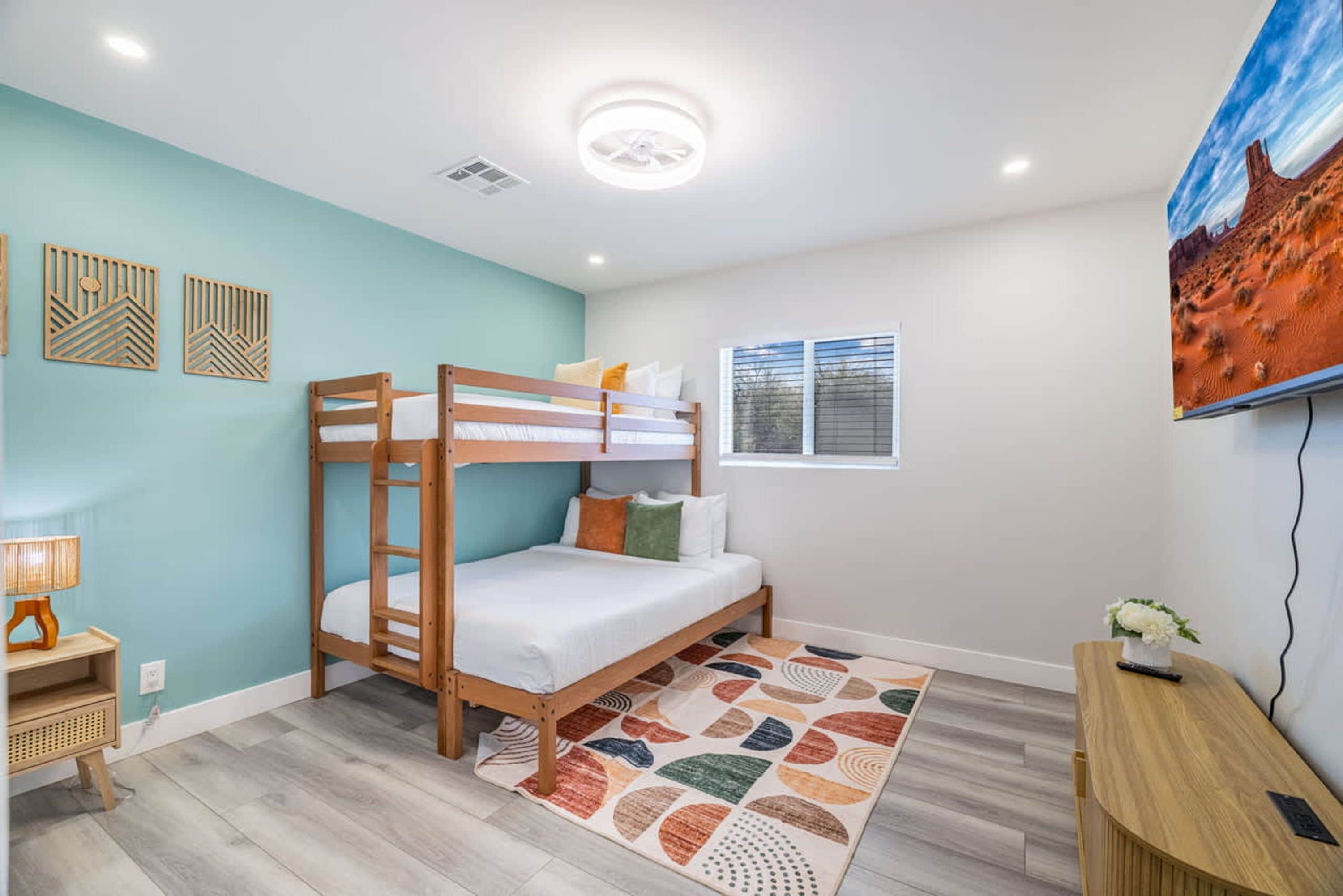 Une chambre avec un lit superposé, un tapis à motifs, un bureau et un téléviseur fixé au mur.