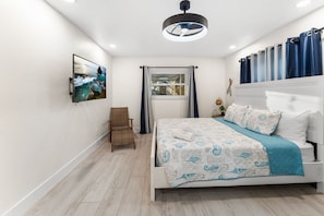 A bedroom with a bed, a chair, a window with curtains, a wall-mounted TV, and a ceiling light fixture. - Private Dock Heated Pool Hot Tub Game Room Fun (Apollo Beach)