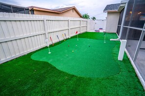 A backyard with artificial green turf, a white fence, and a small putting green with flags. - Private Dock Heated Pool Hot Tub Game Room Fun (Apollo Beach)