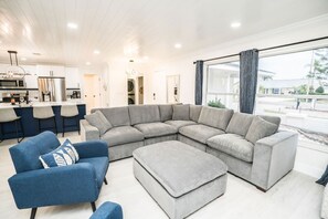 Ein modernes Wohnzimmer mit einem Ecksofa, einem blauen Sessel und einem passenden Hocker.