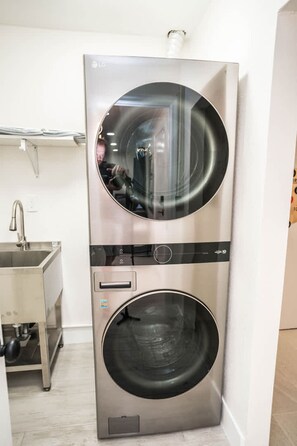 A compact, stainless steel, two-door washer-dryer unit in a modern kitchen with a built-in sink and a towel rack above it. - Private Dock Heated Pool Hot Tub Game Room Fun (Apollo Beach)