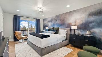 A modern bedroom with a large bed, a view of the outdoors through a window, a dark dresser, and a green chair.