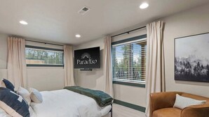 A bedroom with a bed, a TV, a couch, and a painting. - Lakeside Montana Hot Tub Game Room (Lakeside)