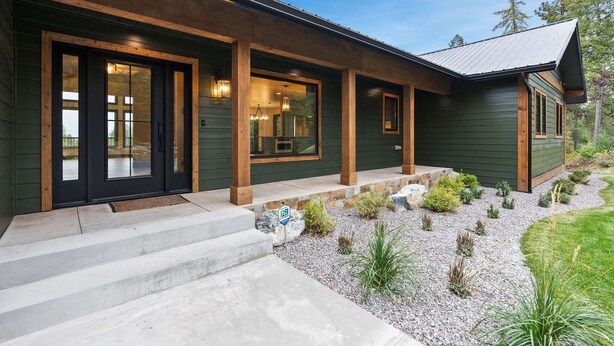 A modern house with a dark green exterior, a front porch with steps, and a gravel driveway. - Lakeside Montana Hot Tub Game Room (Lakeside)
