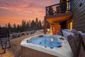 A hot tub on a wooden deck with a view of trees and a sunset. - Lakeside Montana Hot Tub Game Room (Lakeside)